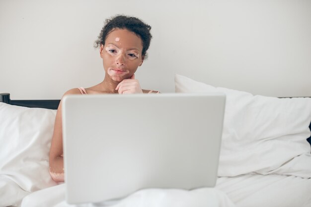 Op internet. Jonge vrouw zit in bed en kijkt naar iets op een laptop