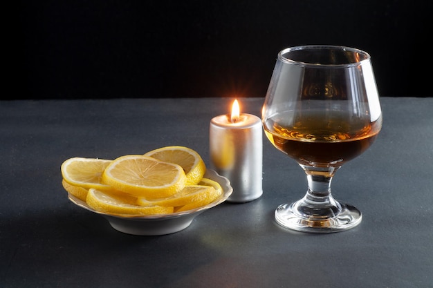 Op tafel staat een glaasje cognac. In de buurt zijn gesneden citroenen in een bord.