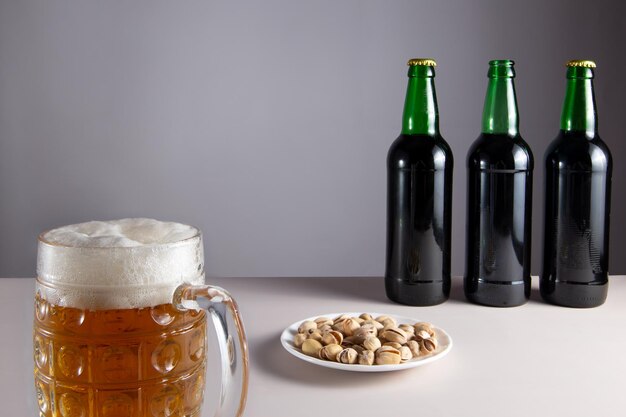 Op tafel staat een glas bier. Daarachter liggen gezouten nootjes en drie flesjes bier.