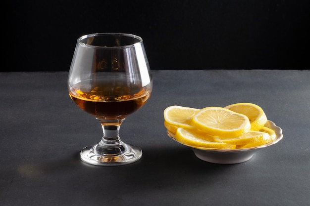 Op tafel staat een glas cognac. Vlakbij staat een bord met gesneden citroenen.