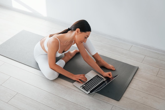 Op yogamat is een jonge blanke vrouw met slanke lichaamsvorm overdag binnenshuis