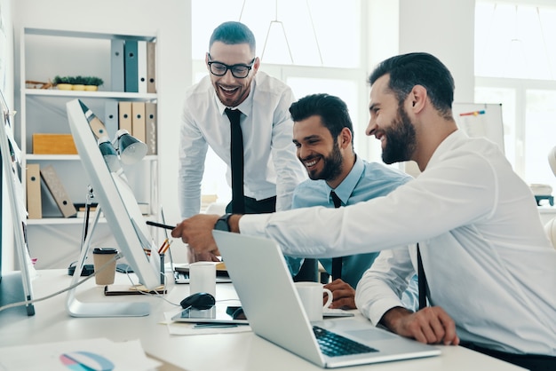 Op zoek naar de juiste beslissing. Groep jonge moderne mannen in formalwear die met computers werken terwijl ze op kantoor zitten