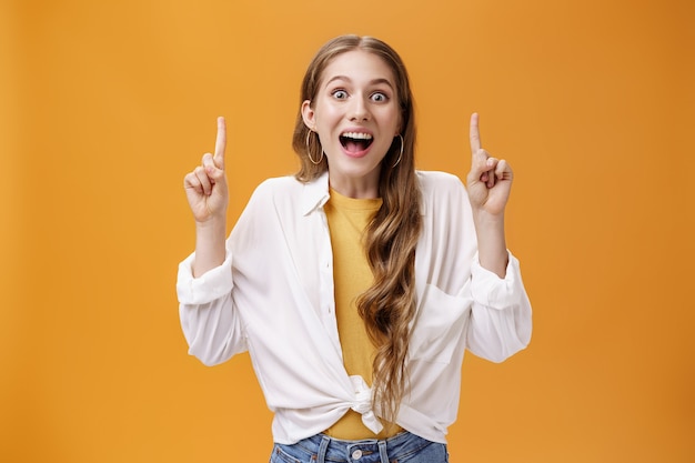 Op zoek naar de zonnige kant. charismatische gelukkige enthousiaste jonge aantrekkelijke vrouw in witte blouse die kaak laat vallen met een brede vrolijke glimlach die omhoog wijst met opgeheven wijsvingers die een geweldig ding laten zien.