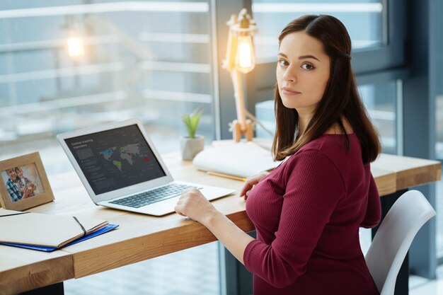 Op zoek naar informatie. Close-up van attente jonge vrouw op zoek naar jou tijdens het gebruik van een laptop en zittend aan tafel