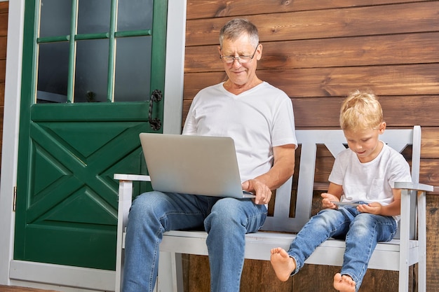 Opa en kleinzoon zitten met gadgets op een bankje bij een houten huis