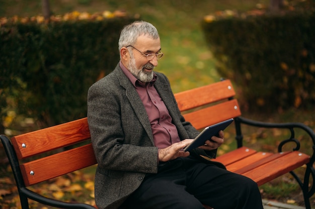 Opa gebruikt een tablet zittend in de pakr op de bank