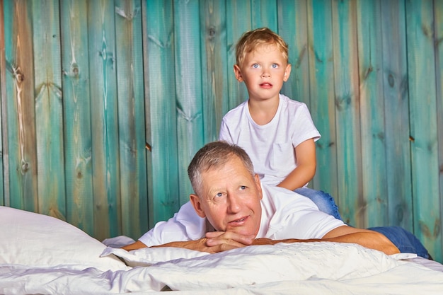 Opa speelt met zijn kleinzoon op het bed twee generaties mannen, een grootvader en een schattige kleinzoon liggen op het bed en genieten van gezamenlijke ontspanning in de slaapkamer