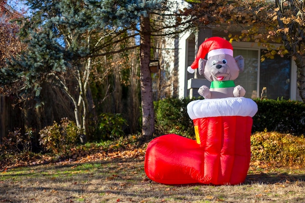 Opblaasbare figuur van rode schoen met hond in kerstmuts erin, staat in het park. Kerstdecor voor buiten