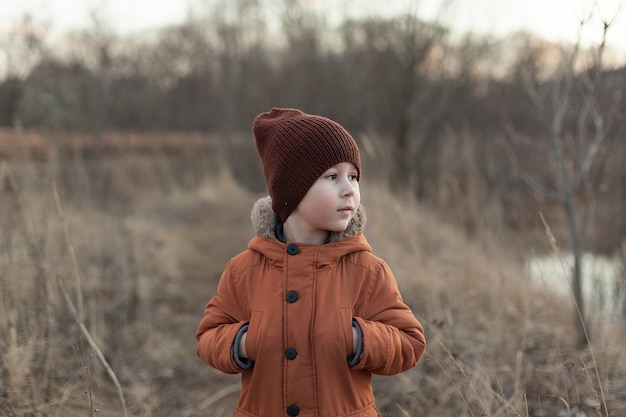 Apra il ritratto di autunno di un ragazzo carino vestito con una giacca marrone e un cappello, un bambino che si diverte nel parco.