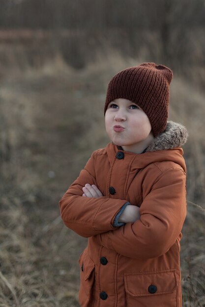 茶色のジャケットと帽子に身を包んだかわいい男の子、公園で楽しんでいる子供の秋の肖像画を開きます。