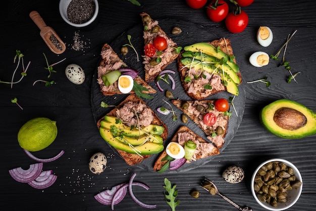 Open avocado sandwiches with tuna on whole grain bread on dark background top view Food recipe background Close up