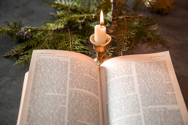 Open Bible, candle and coniferous branches on table