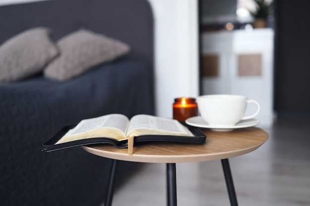 Open Bijbel met een kopje thee en kaarsen op een houten tafel in de slaapkamer. Tijd voor gebed.