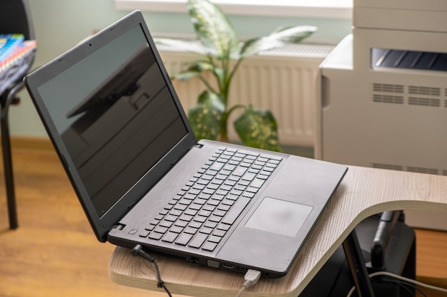 Open black laptop computer on a small chair table in office interior.