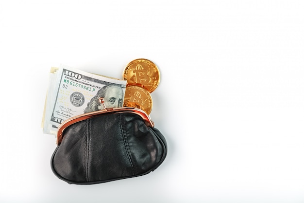 Un portafoglio aperto nero con monete di denaro, dollari e bitcoin su un muro bianco.