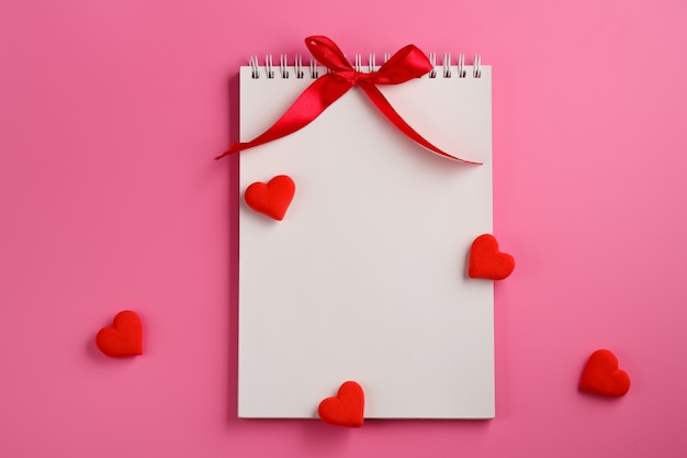 Foto apra il taccuino in bianco, cuore rosso su fondo rosa. san valentino e concetto di vacanza romantica. messaggio d'amore. vista dall'alto, piatto con spazio di copia.