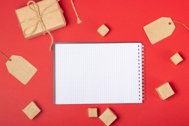 Open blank notebook with place to add text, shopping cart and boxes on a bright red background. Online shopping concept