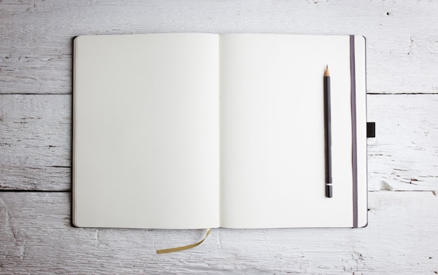 白い木製のテーブルに鉛筆で空のページで空白のメモ帳を開きます