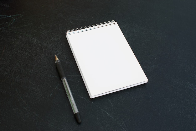 Open blank notepad with a pen next to it on black background