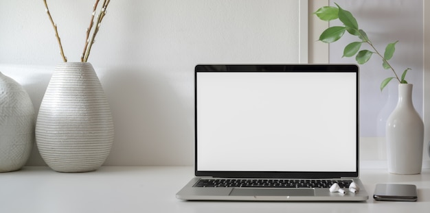 Open blank screen laptop computer in minimal workspace with copy space and ceramic vase 