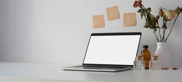 Open blank screen laptop computer with ceramic vase and decorations on white table