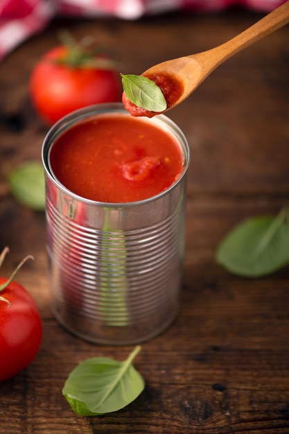 Open blikje tomatensaus met hele verse tomaten op een rustieke houten tafel. Detailopname