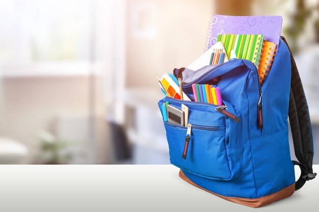 Open blue school backpack on a wooden desk and bokeh background.