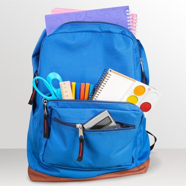 Open blue school backpack on wooden desk and gray background.