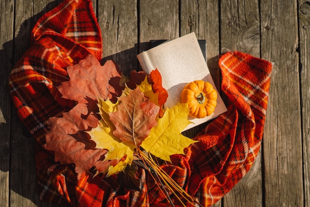 Open boek met oranje pompoenboeket van herfstbladeren met een plaid op een houten ondergrond