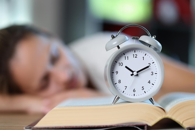 Open book and alarm clock close up sleeping woman in background concept of overstudy overwork