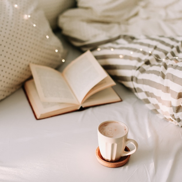 Open book on bedsheets and a cup of coffee