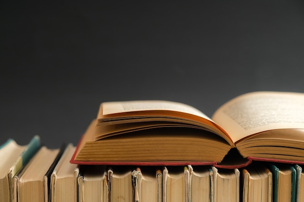 Open book on black surface, hardback books on wooden table.