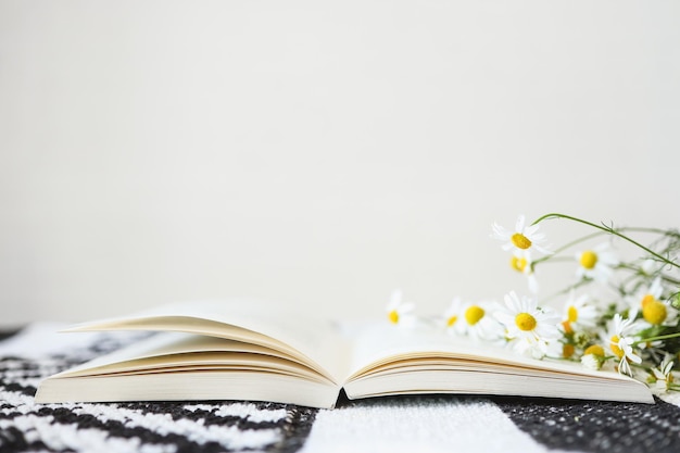 An open book and a bouquet of daisies on a table