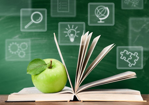 open book, green apple and digital holograms on chalkboard background