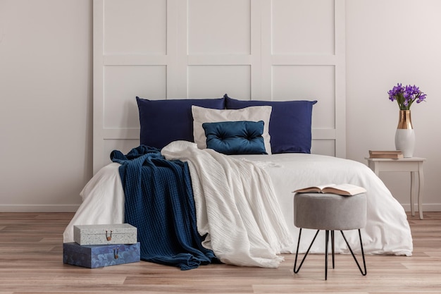 白と青の寝具を備えたキングサイズベッドの前にある灰色のパウフのオープンブック