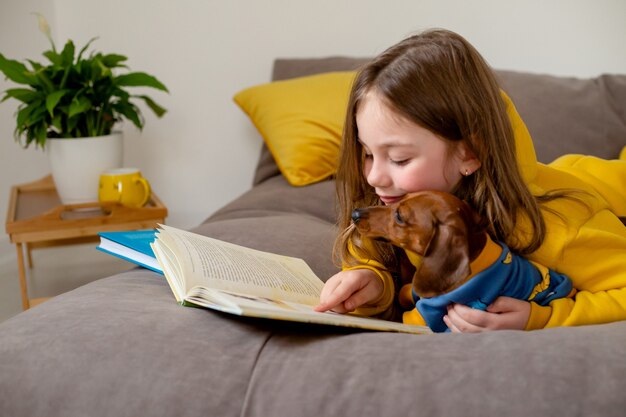 開いた本はベッドに横たわっています子供は学校で遊んでいて、犬に高品質の写真を読むように教えています