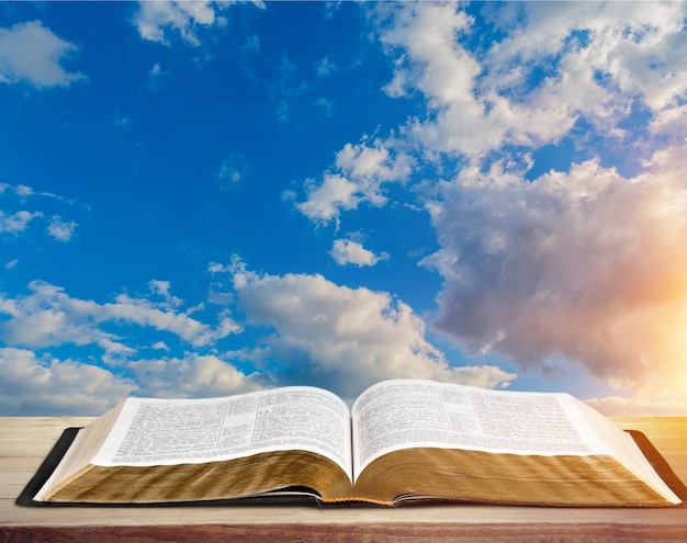 Open book on old wooden table on sky background sunlit