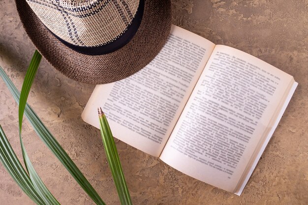 Foto libro aperto, cappello di paglia, foglie di palma su fondo sabbioso