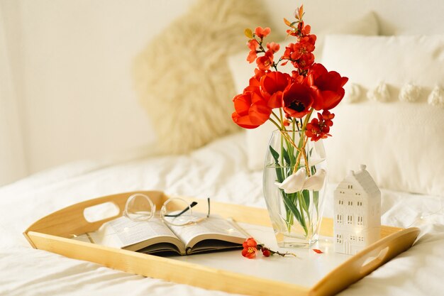 ベッドのトレイに本と花瓶の赤いチューリップを開きます