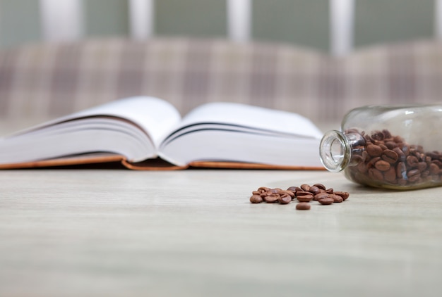 An open book on a white table and a bottle of coffee grains