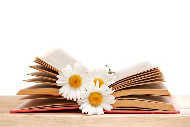 Open book with chamomile flowers on table isolated on white background