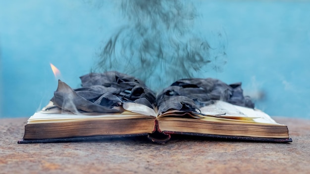 An open book with charred pages and smoke from burning