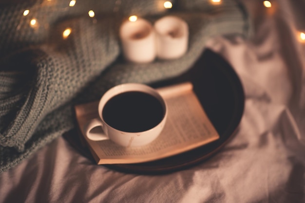 Open book with cup of coffee and knitted sweater in bed at night. Good morning. Breakfast. Cozy evening.