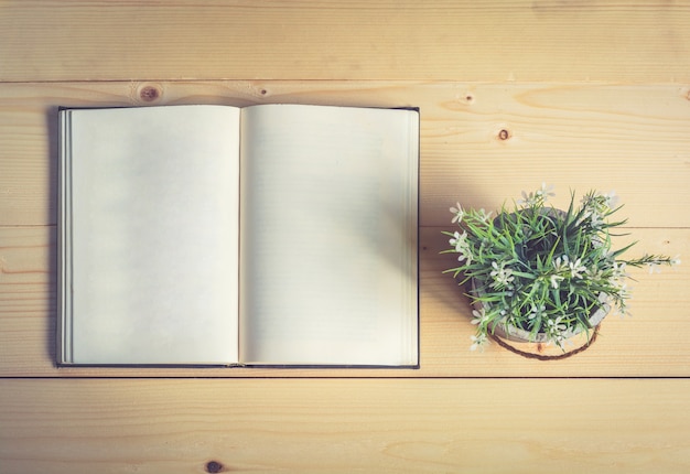 Open book with flower vase on wooden table 