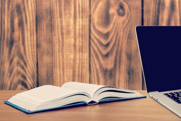 Open book with laptop on wooden table