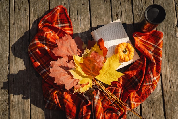 Foto libro aperto con un mazzo di zucca arancione di foglie autunnali con un plaid su uno sfondo di legno