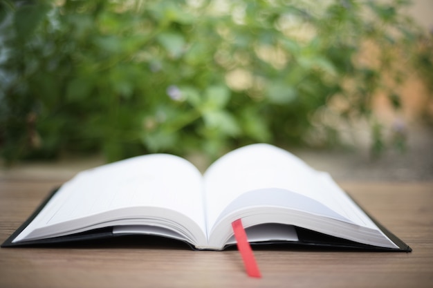 An open book on  wooden table at home garden with nature bokeh background