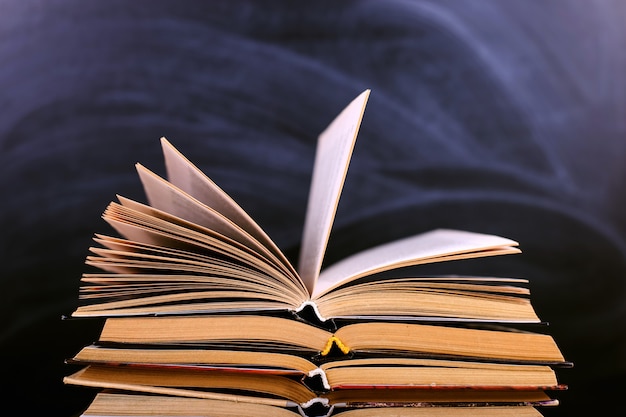 Open books are a stack on the desk, against the background of a chalk board