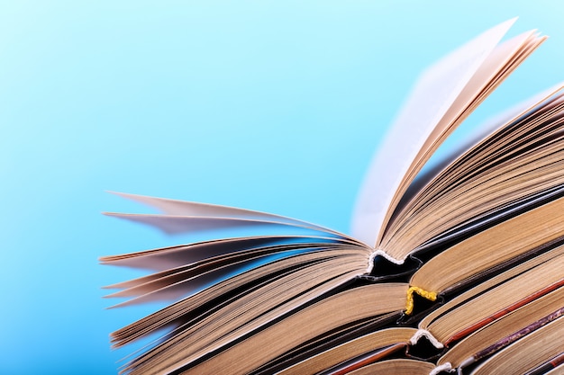 Open books are stacked on the desk on blue. Difficult homework at school, a mountain of knowledge.