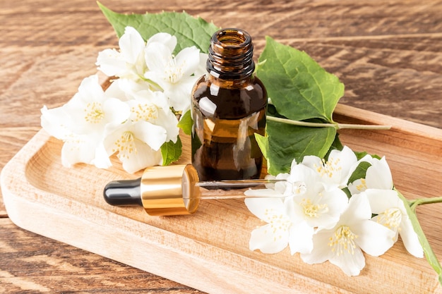 An open bottle of jasmine serum and a pipette filled with a cosmetic natural facial skin care product vitamin AE wooden background
